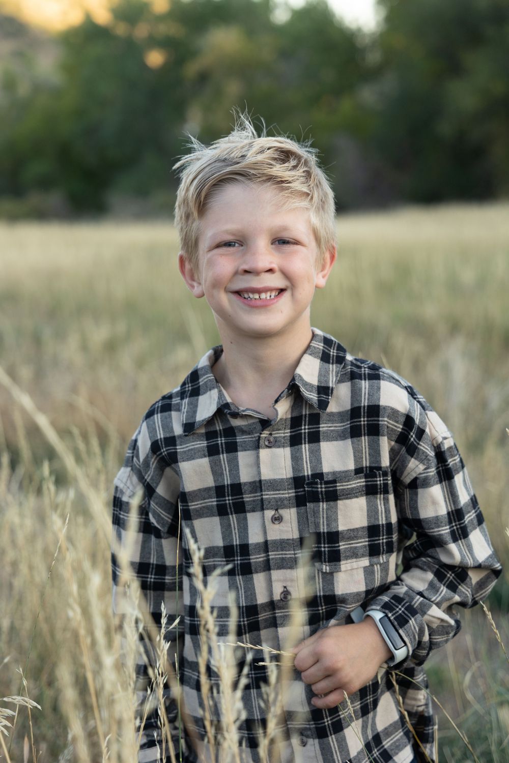 Portrait in a field of tall grass wearing a black and white plaid flannel shirt on a sunny day.