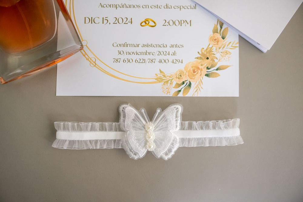 White lace garter and wedding invitation detail shot on gray surface.
