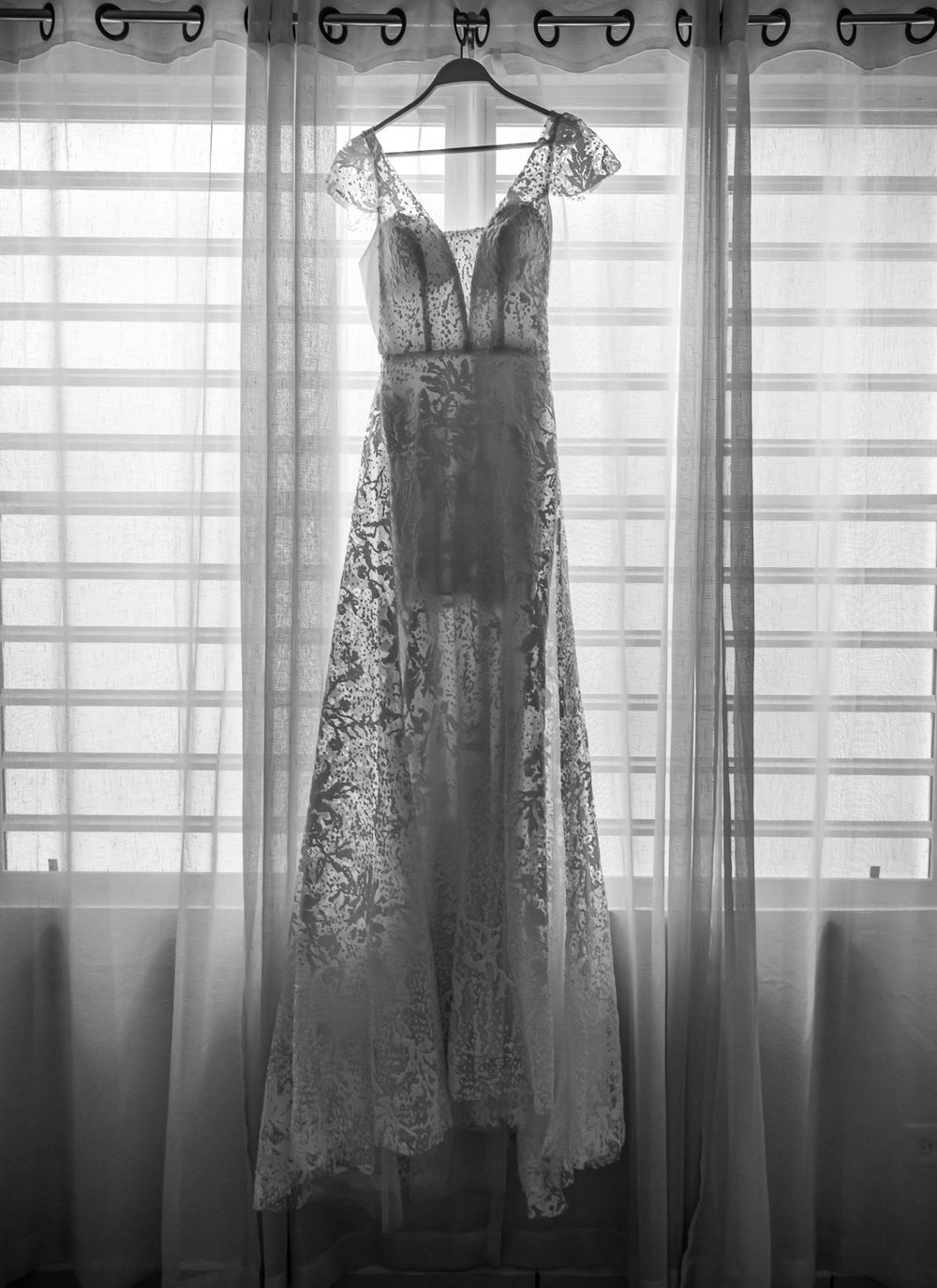 Delicate lace wedding dresses hanging in silhouette against a window with natural light.
