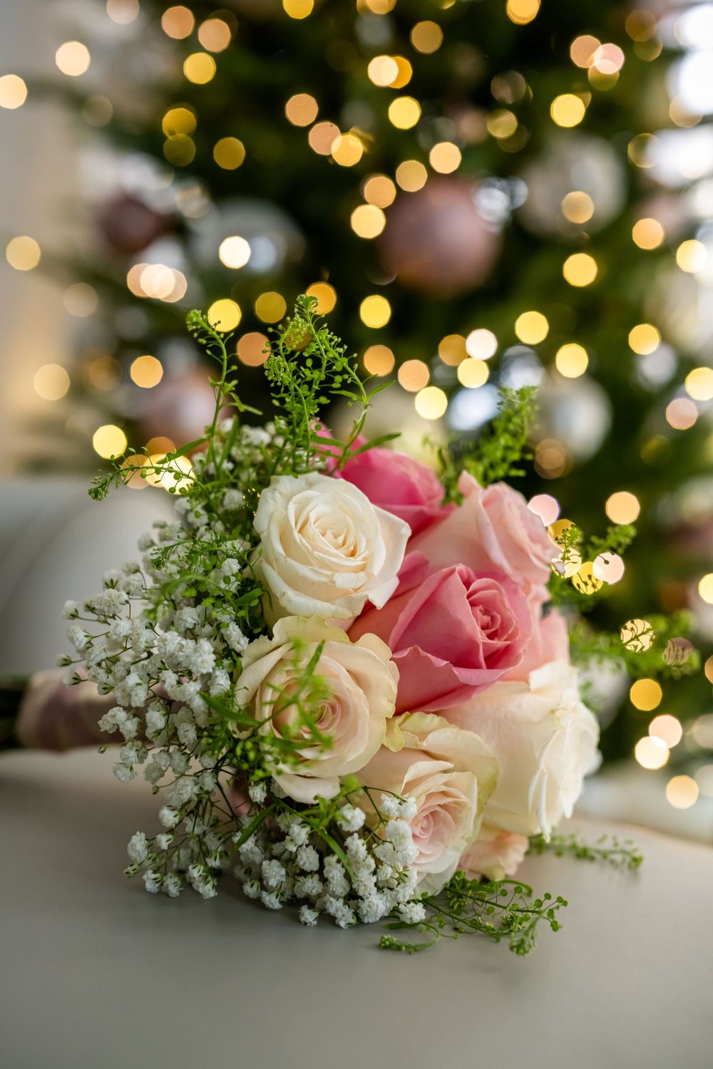 Pink and cream roses with baby's breath arranged against a bokeh light background.