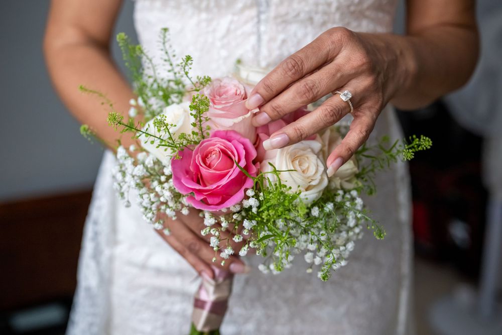 Close-up of bridal bouquet with pink roses and baby's breath held against white lace.