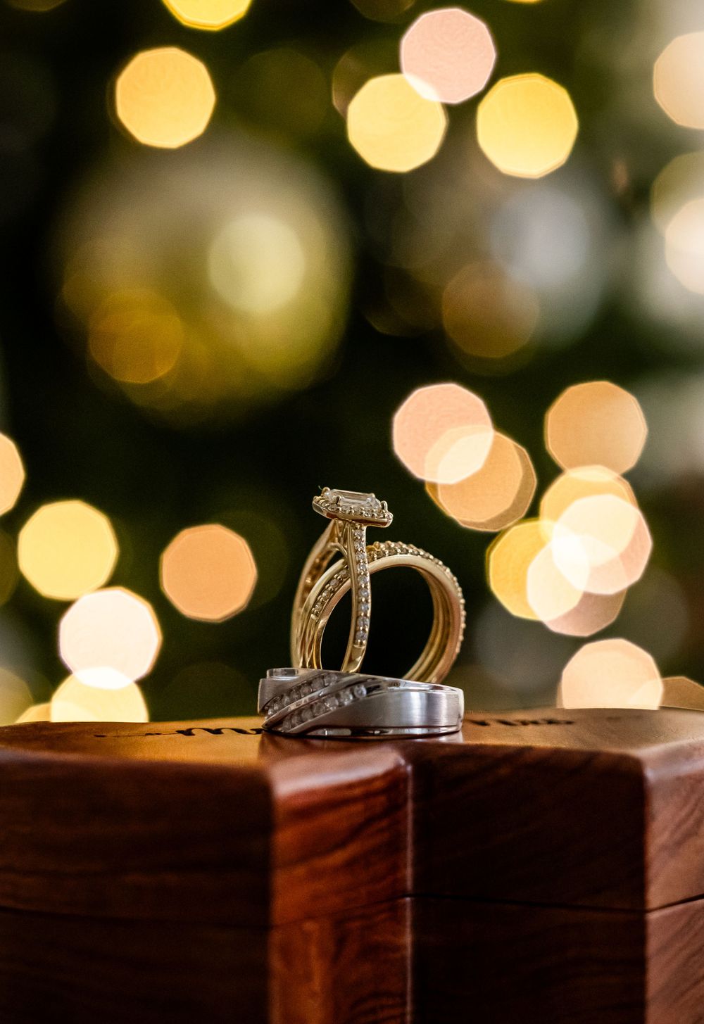 Wedding rings displayed on wooden surface with bokeh lights in background.