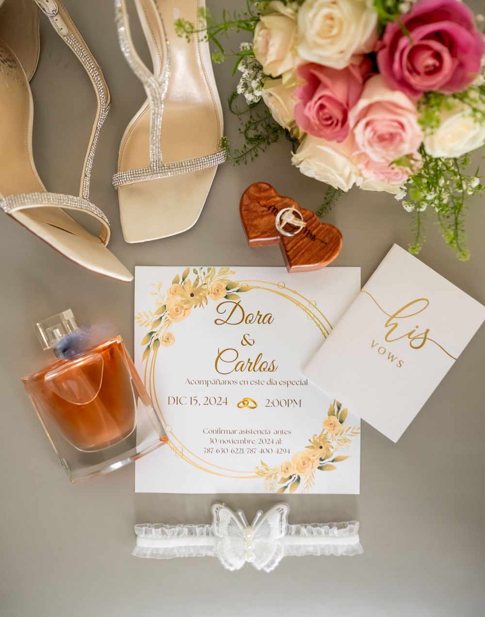 Wedding invitation with roses, perfume, and bridal shoes arranged in flat lay composition.