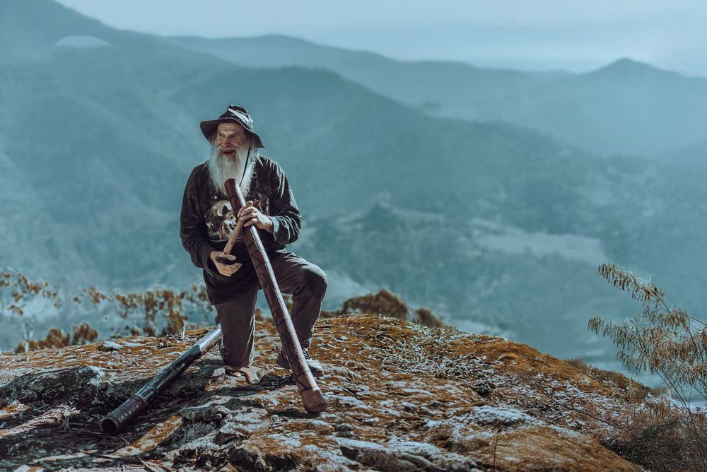 Adventurous hiker stands atop a rocky mountain summit overlooking misty blue peaks in the distance.