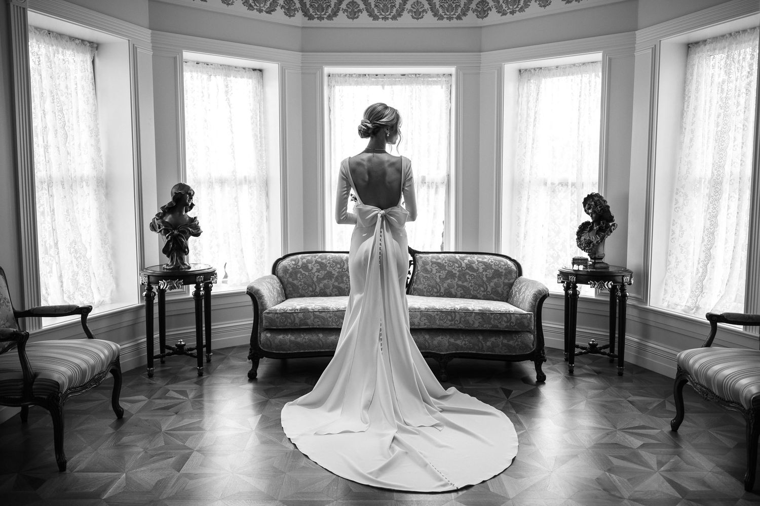 Elegant back view of bride in fitted wedding gown standing in vintage parlor.