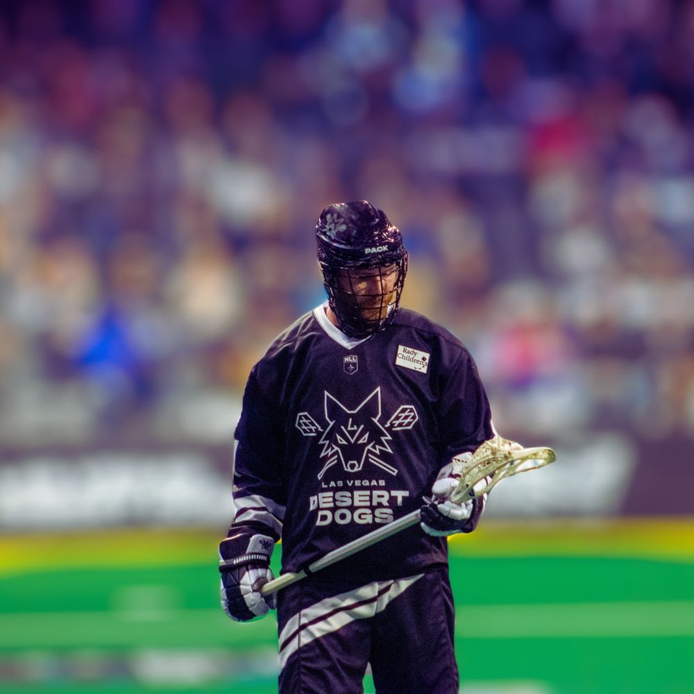 Las Vegas Desert Dogs lacrosse player in dark uniform holding stick during NLL game.