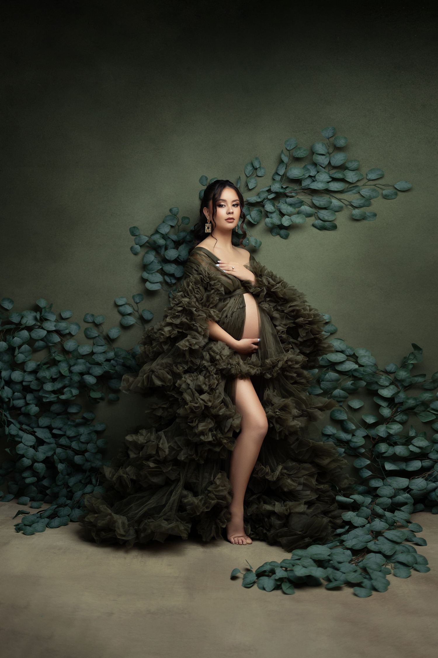 Artistic portrait featuring a dramatic ruffled dark gown against a moody backdrop with blue-green eucalyptus leaves.