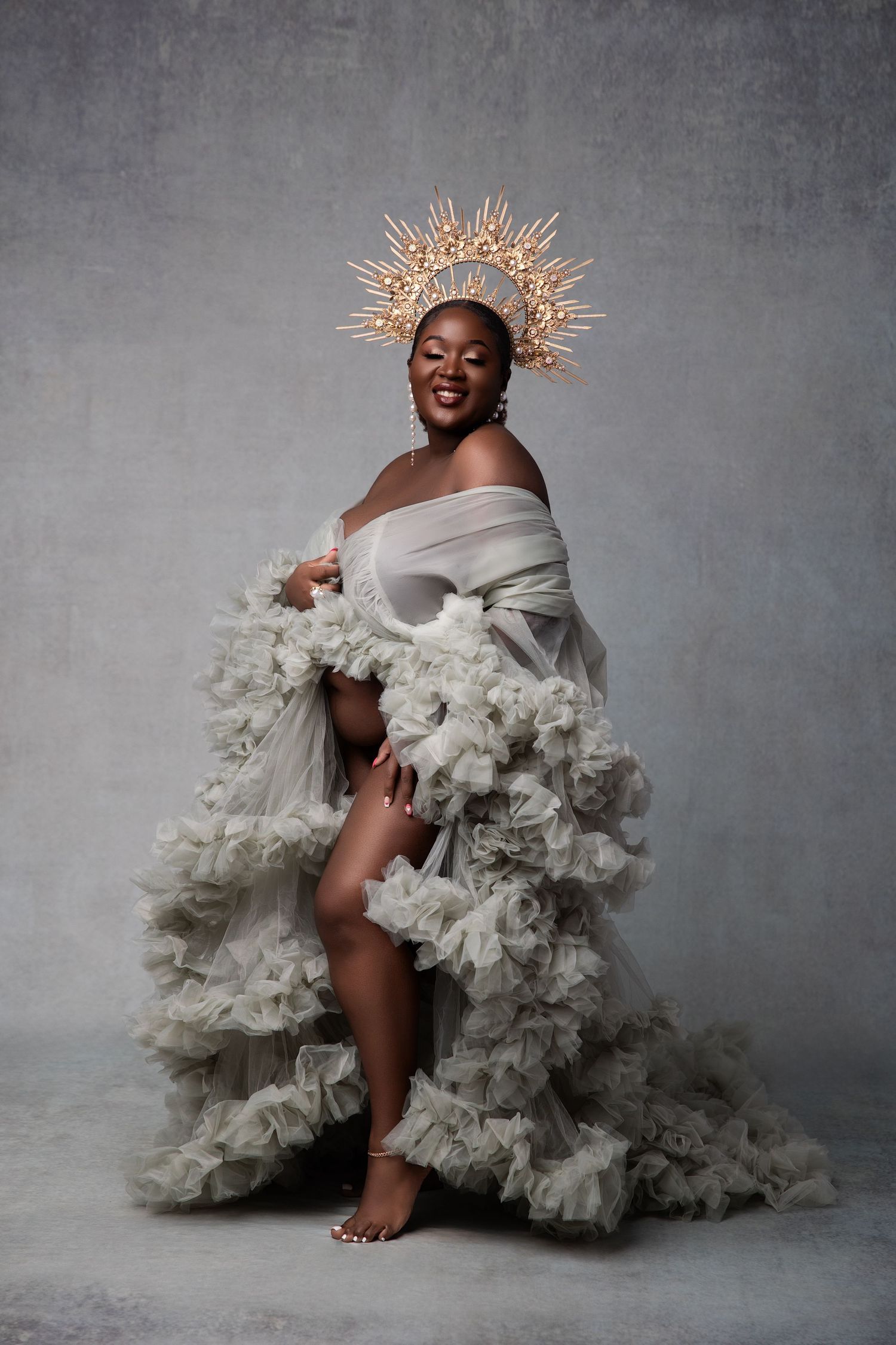 Artistic fashion portrait featuring dramatic white ruffled gown and golden crown-like headpiece against gray backdrop.