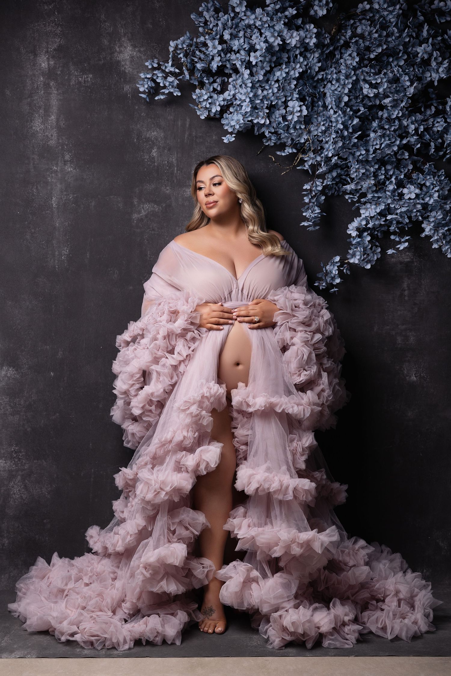 Glamorous fashion shoot featuring flowing pink ruffled robe against dark wall with blue floral decor.