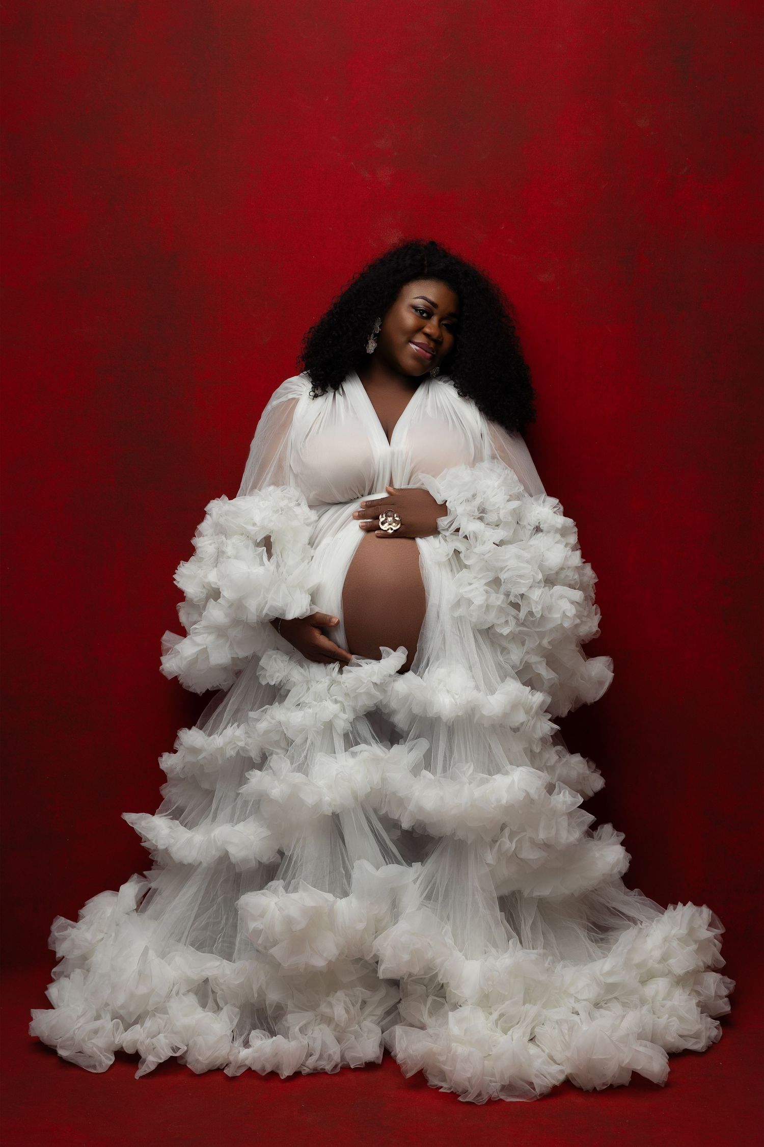 A beautiful maternity photoshoot with a flowing white tulle gown against a rich red backdrop.