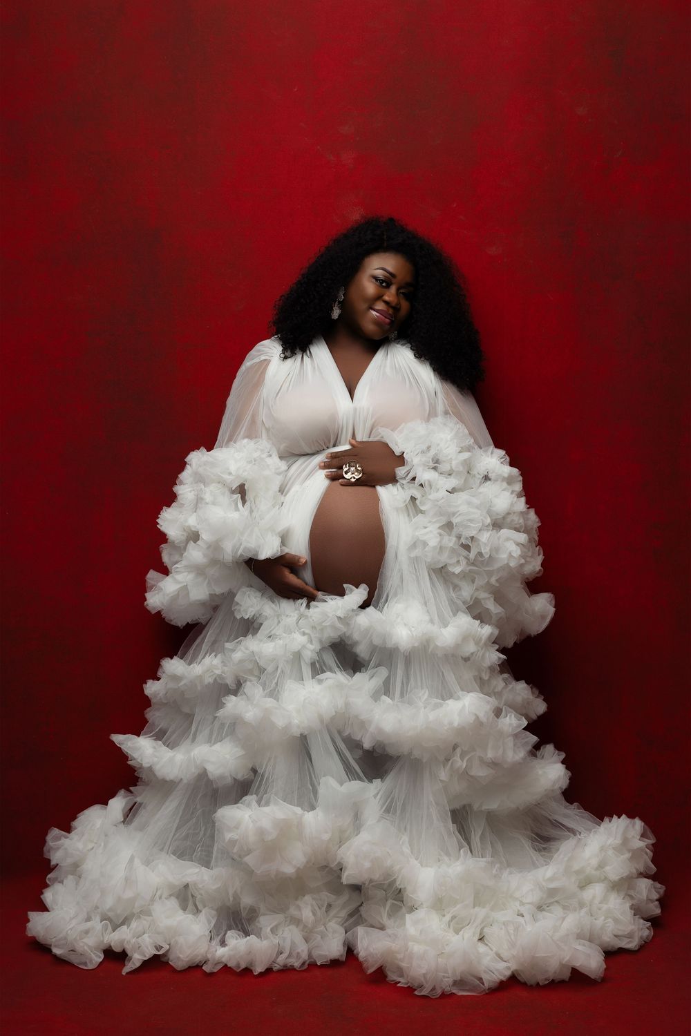 A beautiful maternity photoshoot with a flowing white tulle gown against a rich red backdrop.