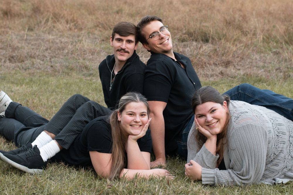 Four people lay casually in the grass for a relaxed outdoor group photo.