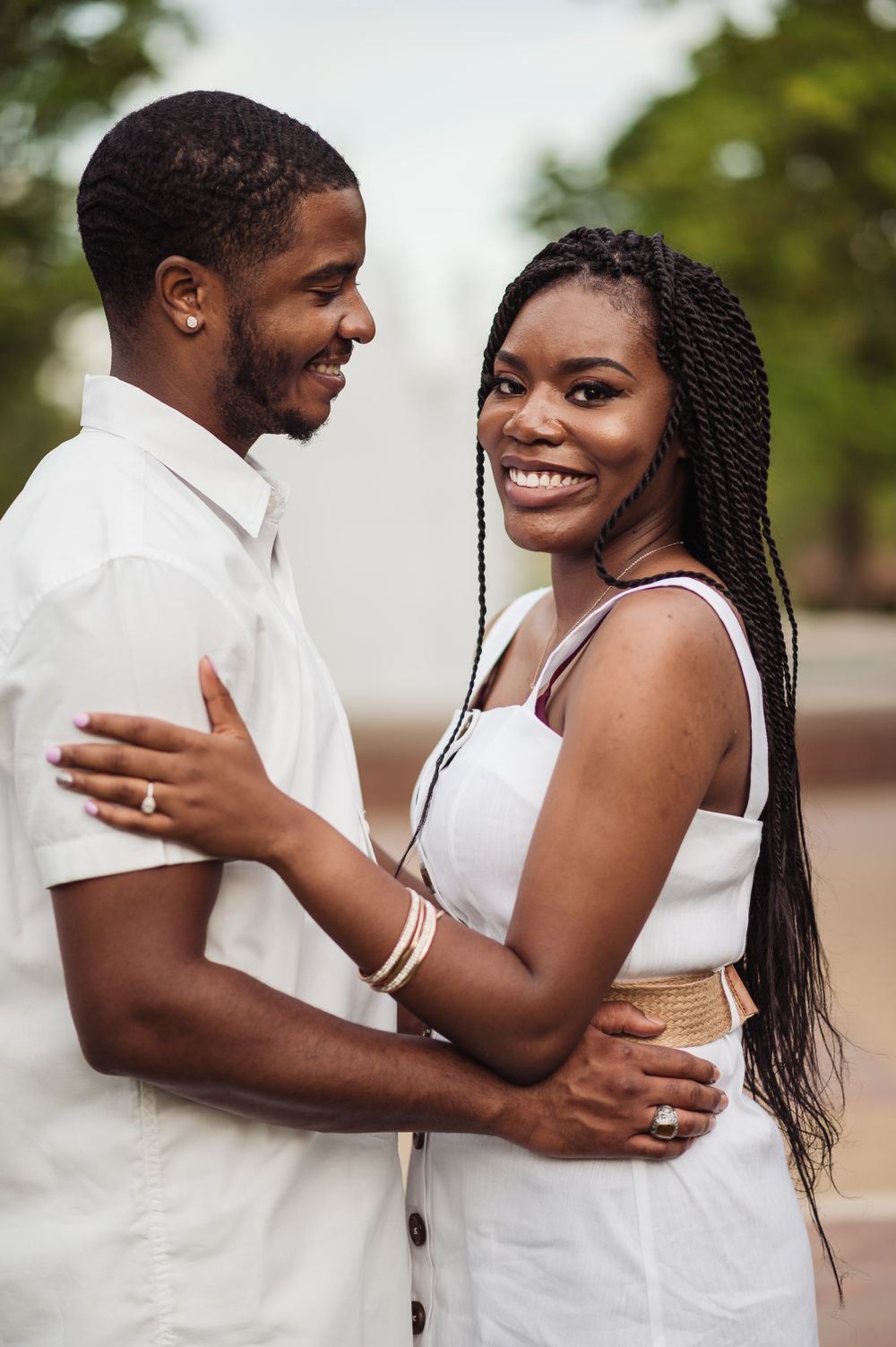Couple in white outfits embracing and smiling outdoors.