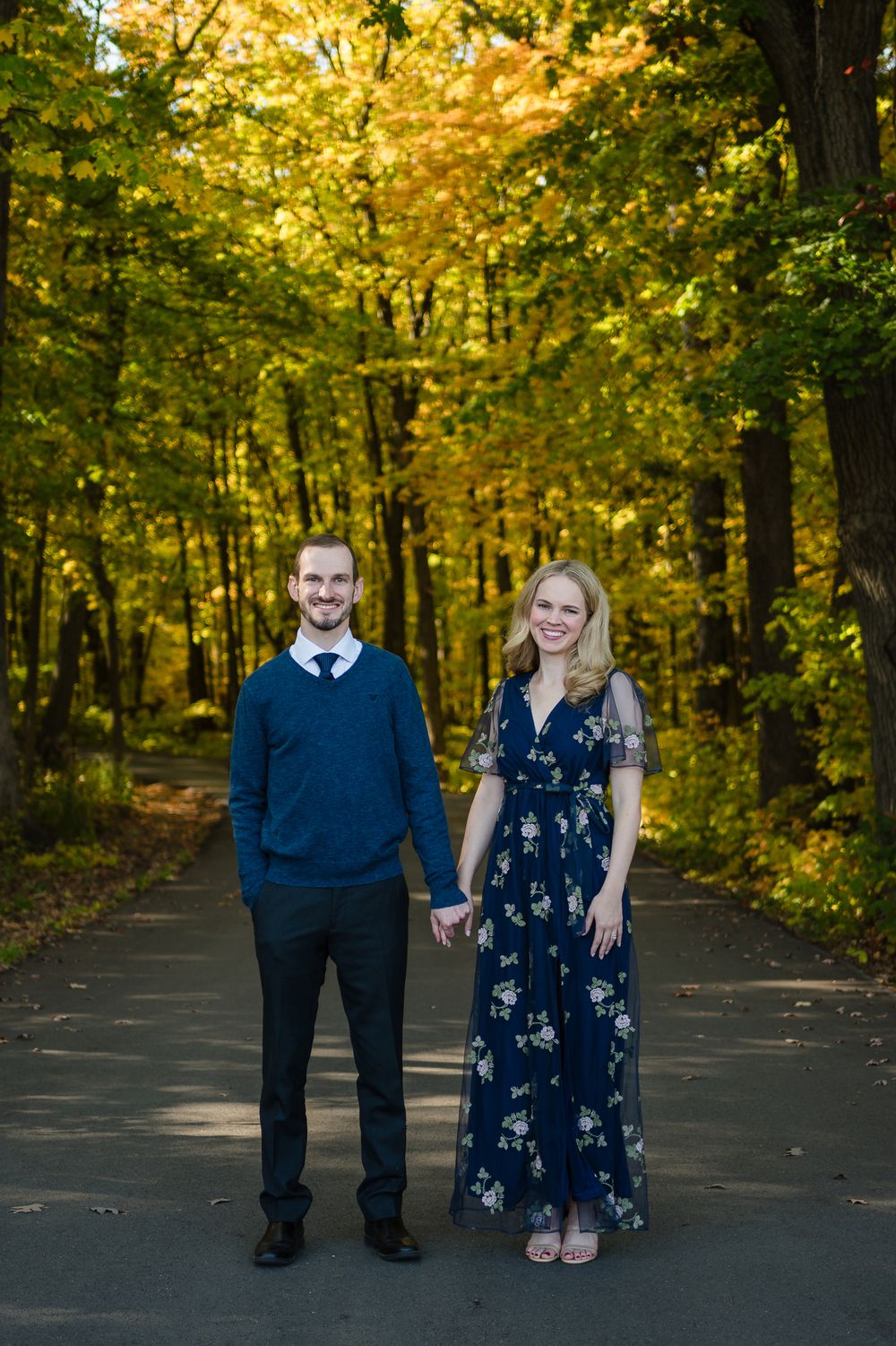 Couple poses on autumn forest path with golden foliage in background.