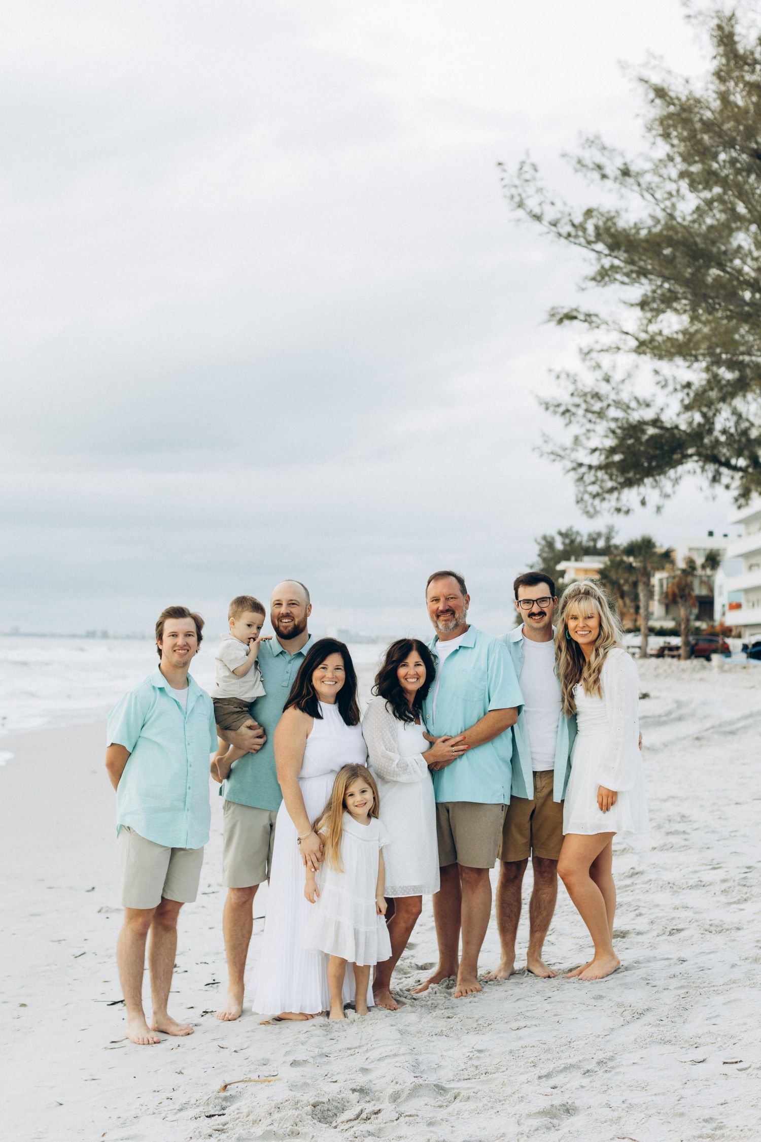 Group photo of family in coordinated white and aqua outfits on sunny beach.