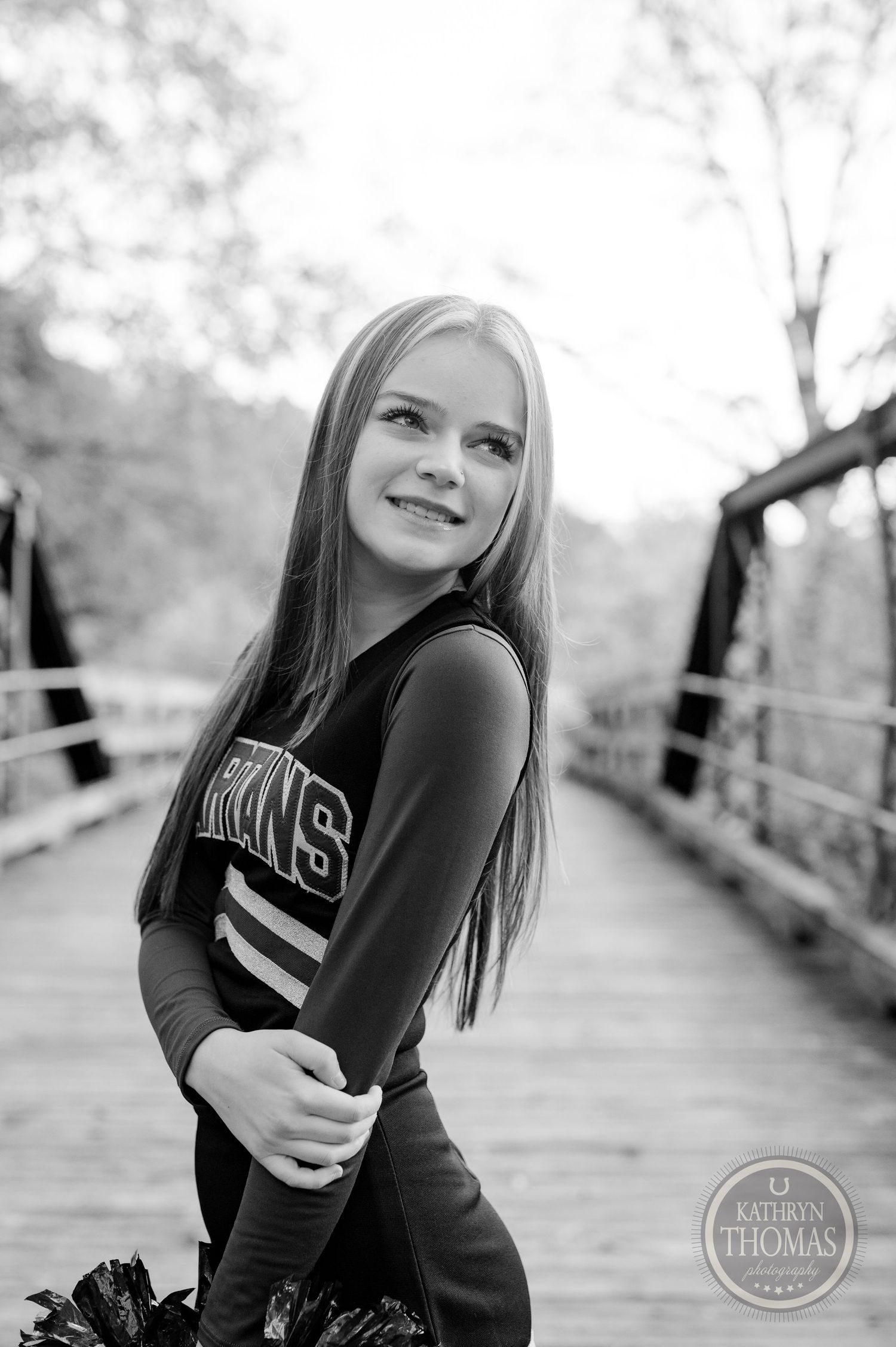 Black and white portrait of cheerleader in uniform on wooden bridge with natural lighting.