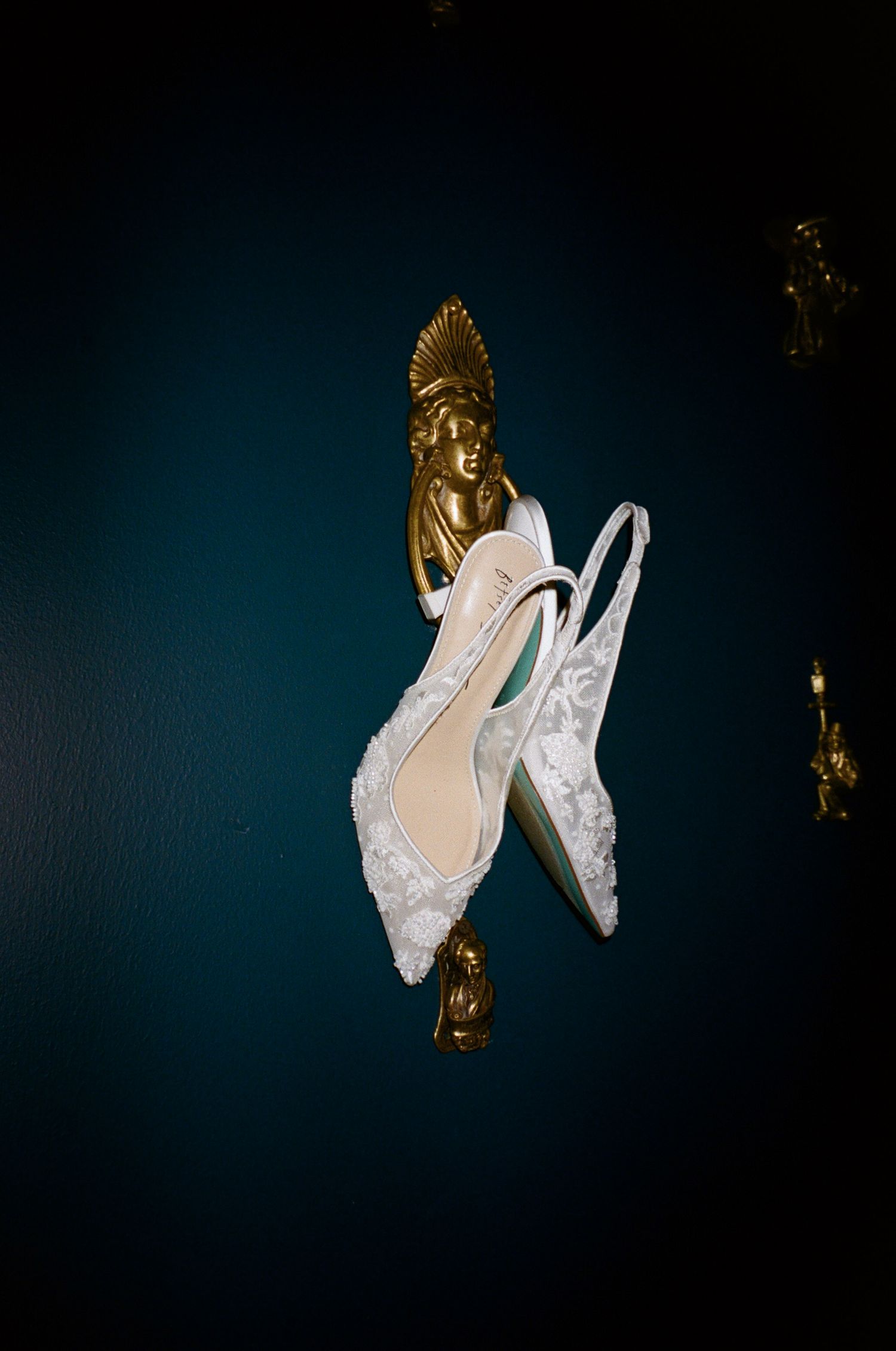 White lace wedding shoes displayed against a dark blue background with gold decor.