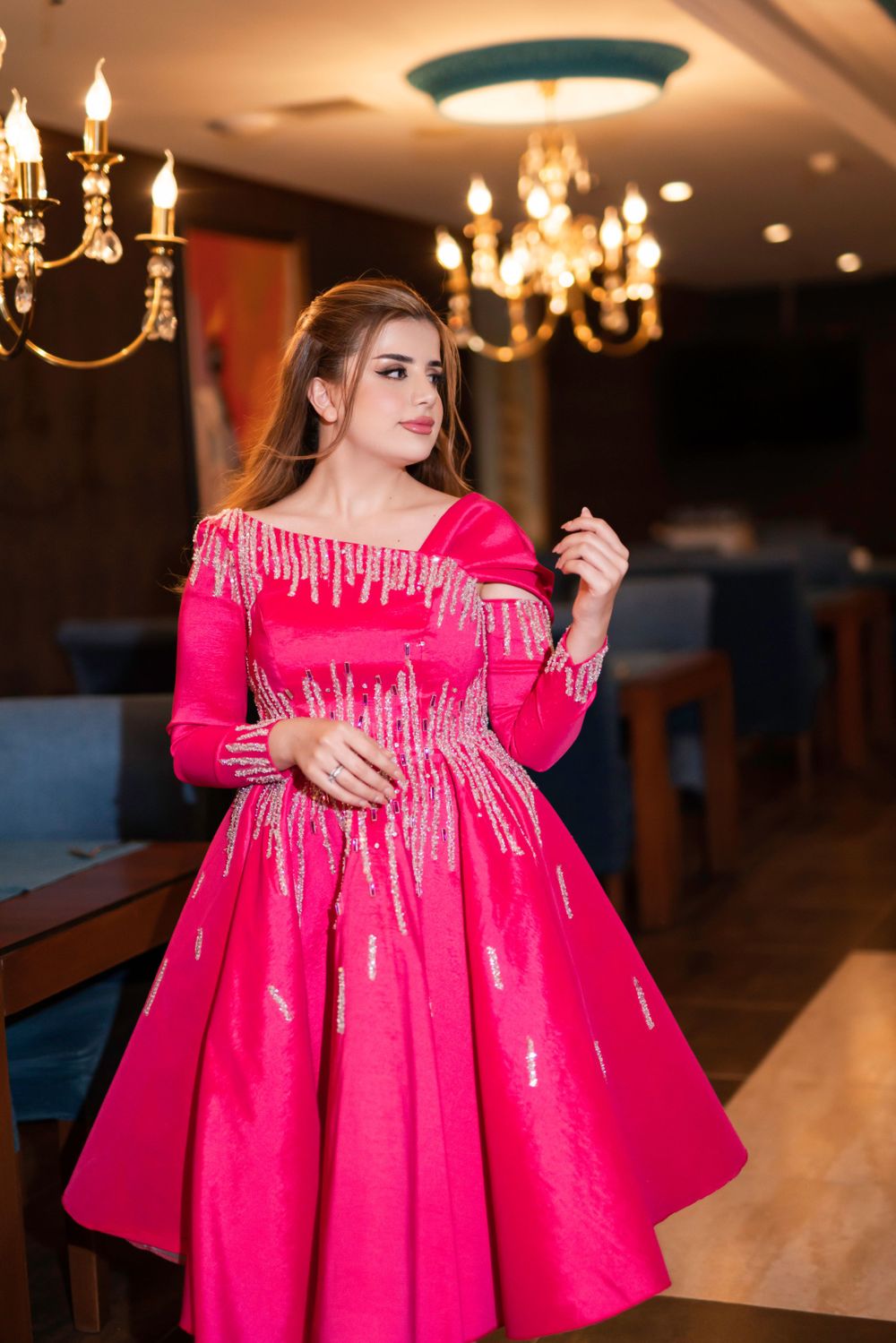An elegant bright pink full-skirted dress with sparkly beaded details and long sleeves sparkles under crystal chandeliers.
