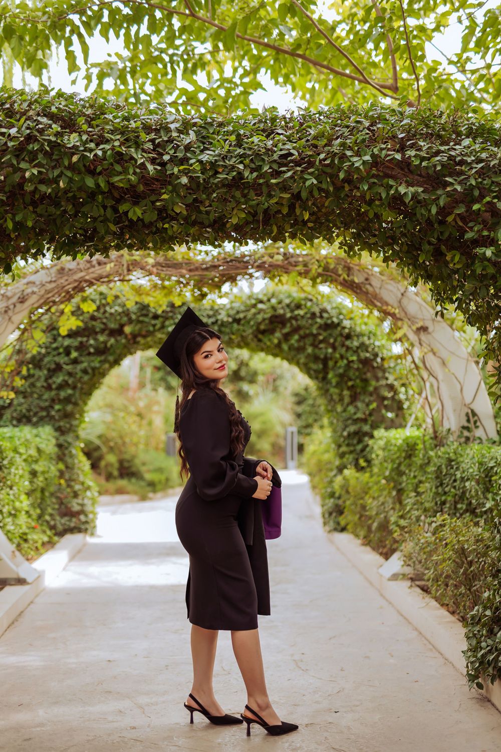 A garden archway covered in lush green vines creates a beautiful tunnel effect over a concrete pathway.