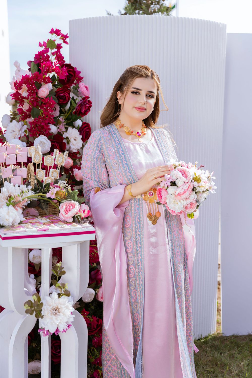Elegant pink and silver embroidered traditional dress displayed with floral arrangements and decor elements.