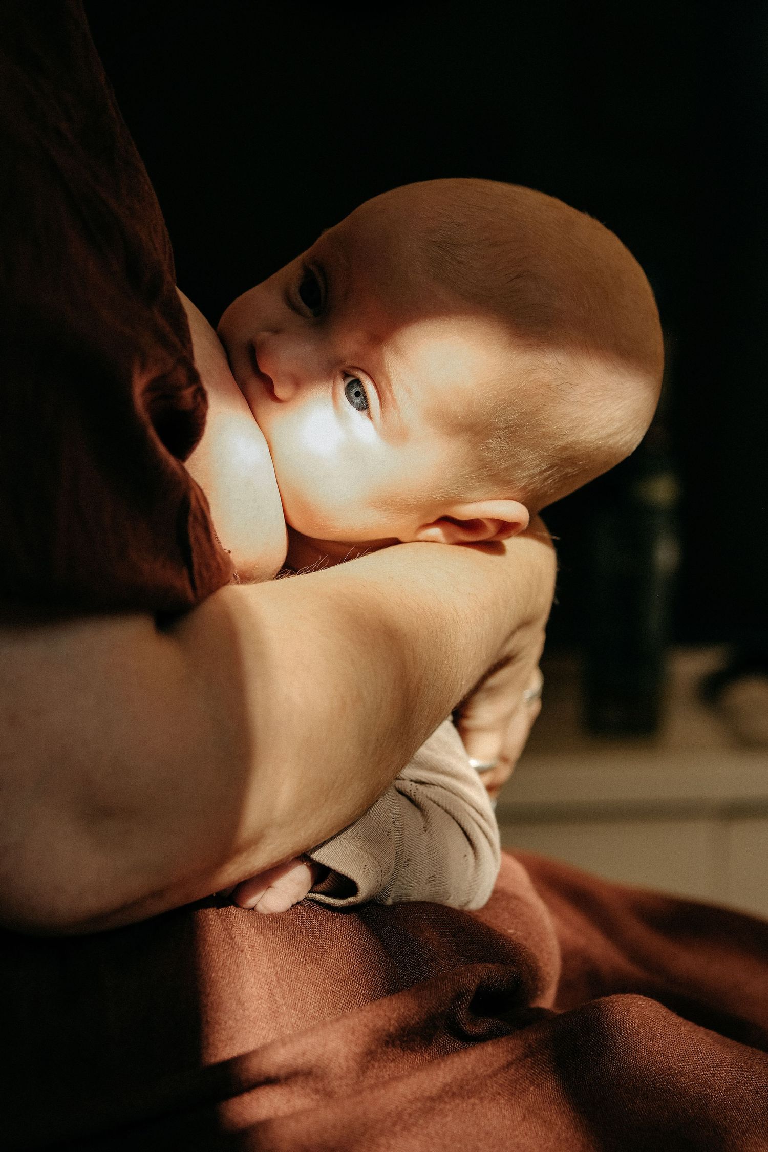 A small infant nursing in soft warm lighting against a dark brown background.