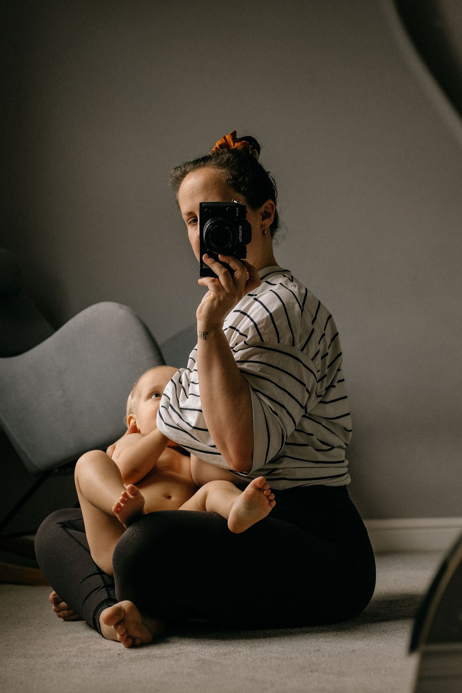 A parent taking a photo while sitting on the floor holding a baby in a striped shirt.