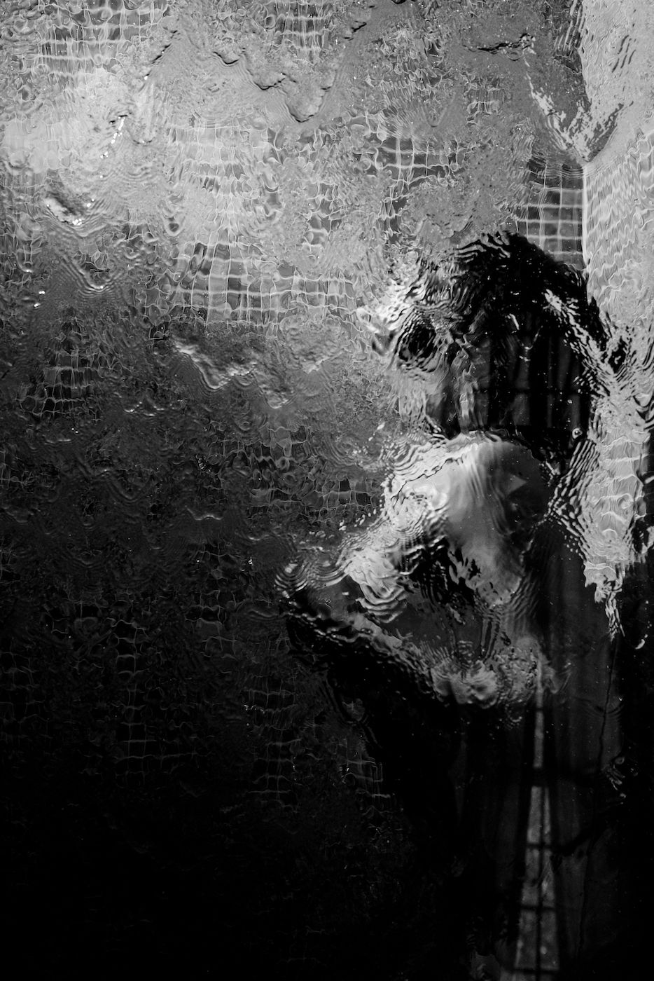 Artistic black and white portrait through textured glass showing distorted silhouette against dark background.