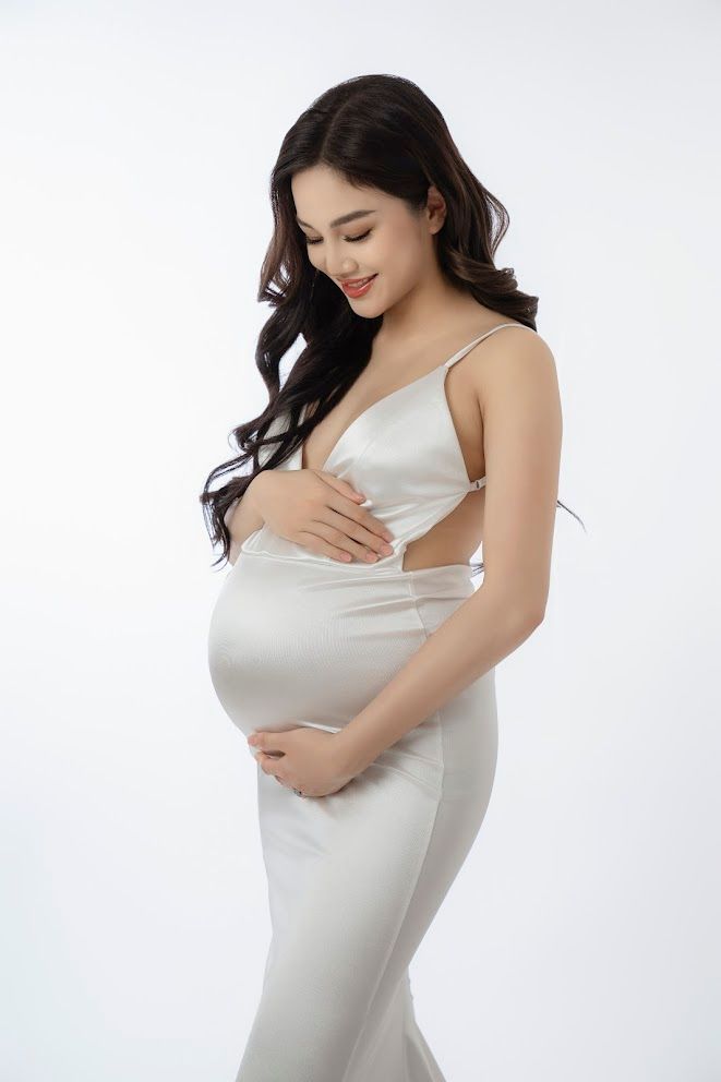 Side profile of figure in white fitted maternity gown against plain white background.