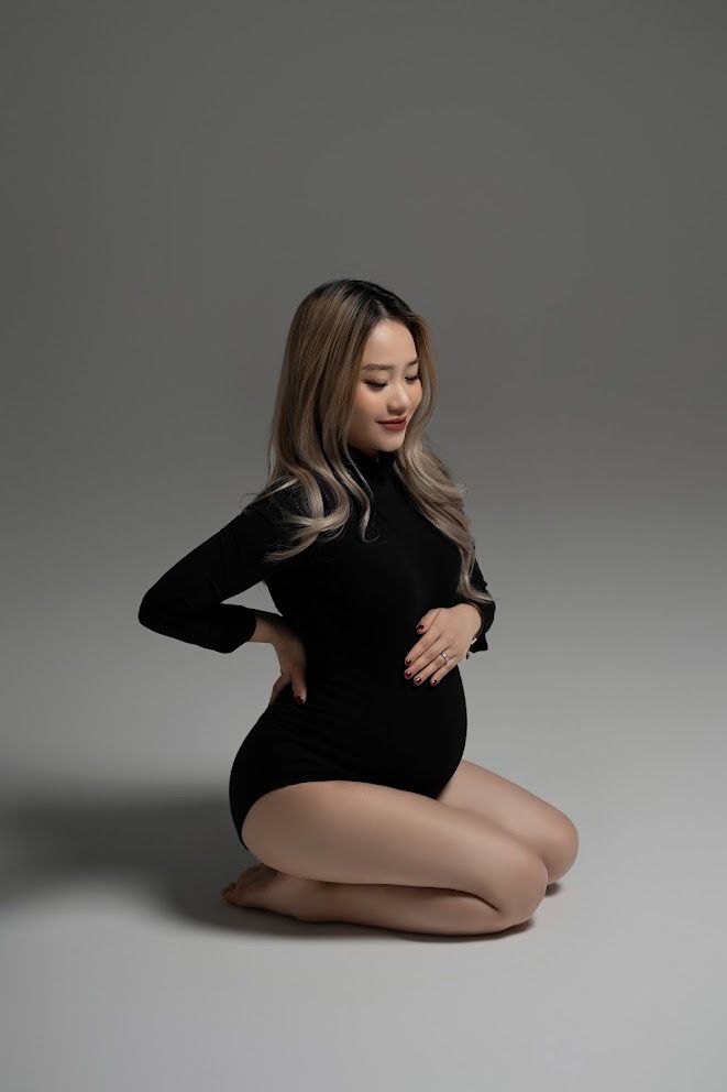 Minimalist maternity portrait in black bodysuit against grey studio background.