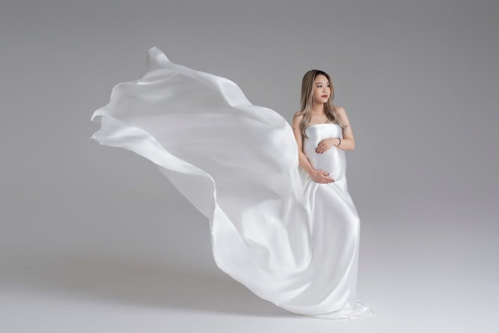 Elegant maternity portrait with flowing white fabric against grey backdrop.