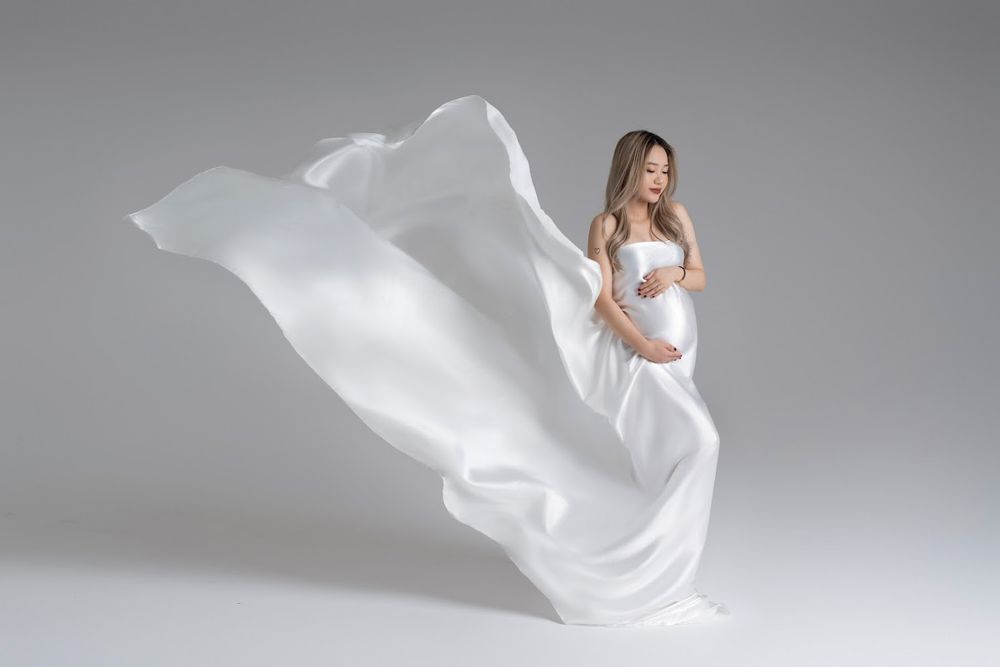 Maternity photo featuring flowing white fabric dramatically billowing around expecting mother in studio setting.