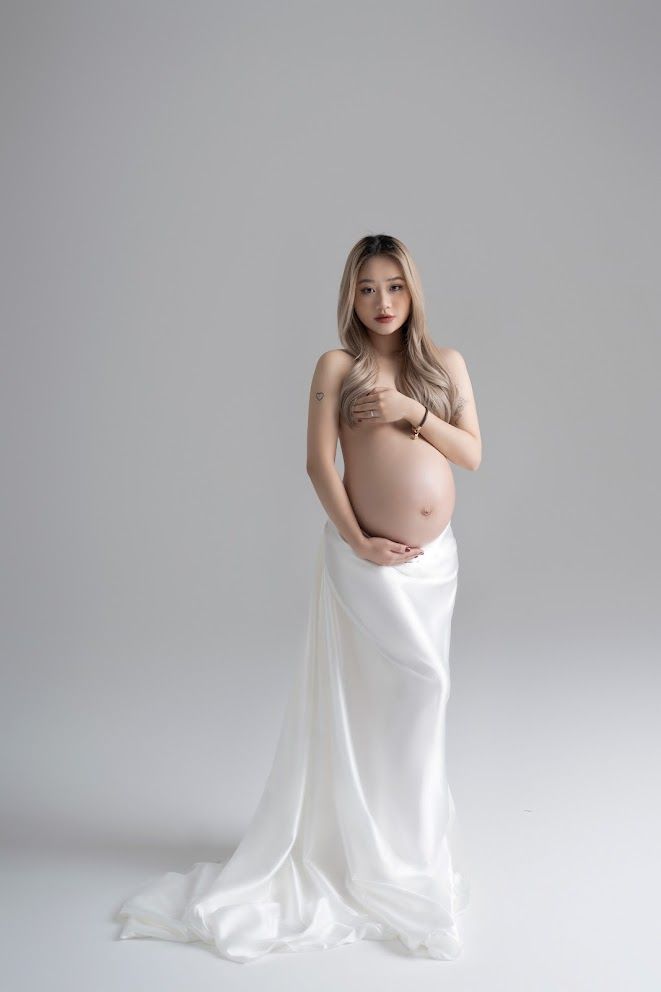 Minimalist maternity photo with white flowing fabric against simple grey backdrop.