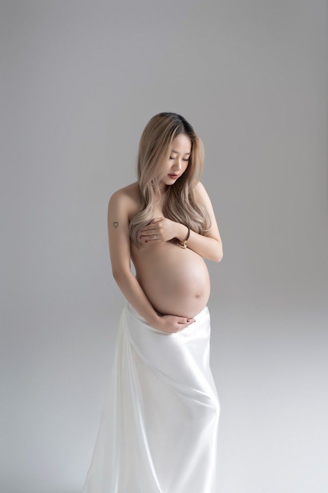 Artistic maternity portrait with white fabric draping against grey studio background.