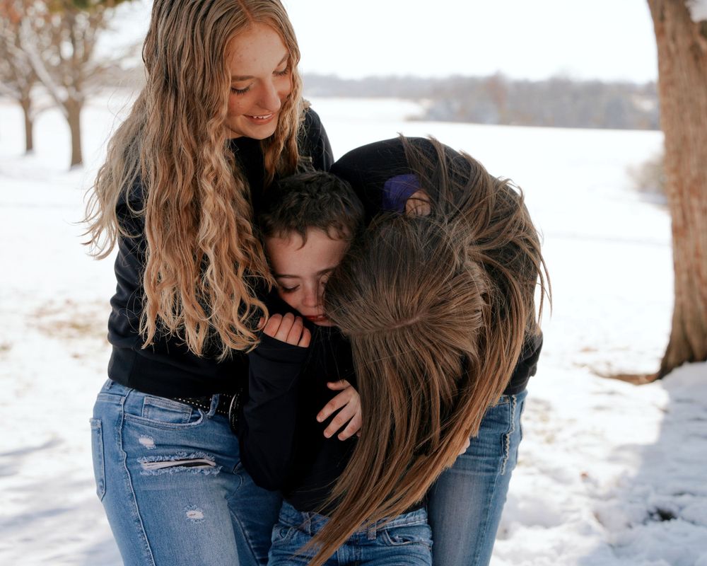 Three siblings sharing a warm group hug in a snowy winter outdoor setting.