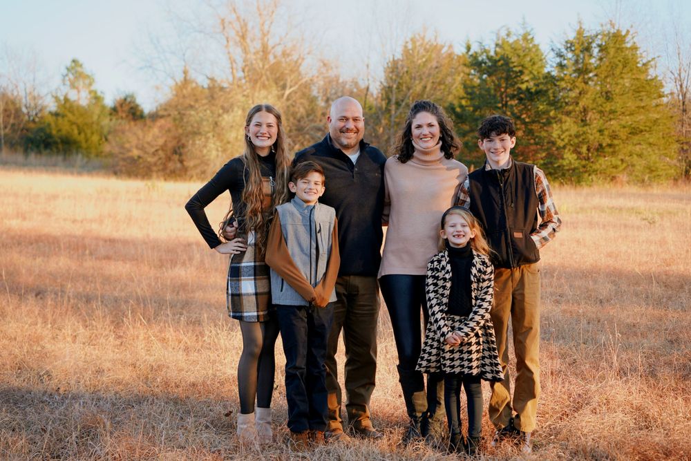 Family of six posing together in a golden autumn field during an outdoor fall photo session.