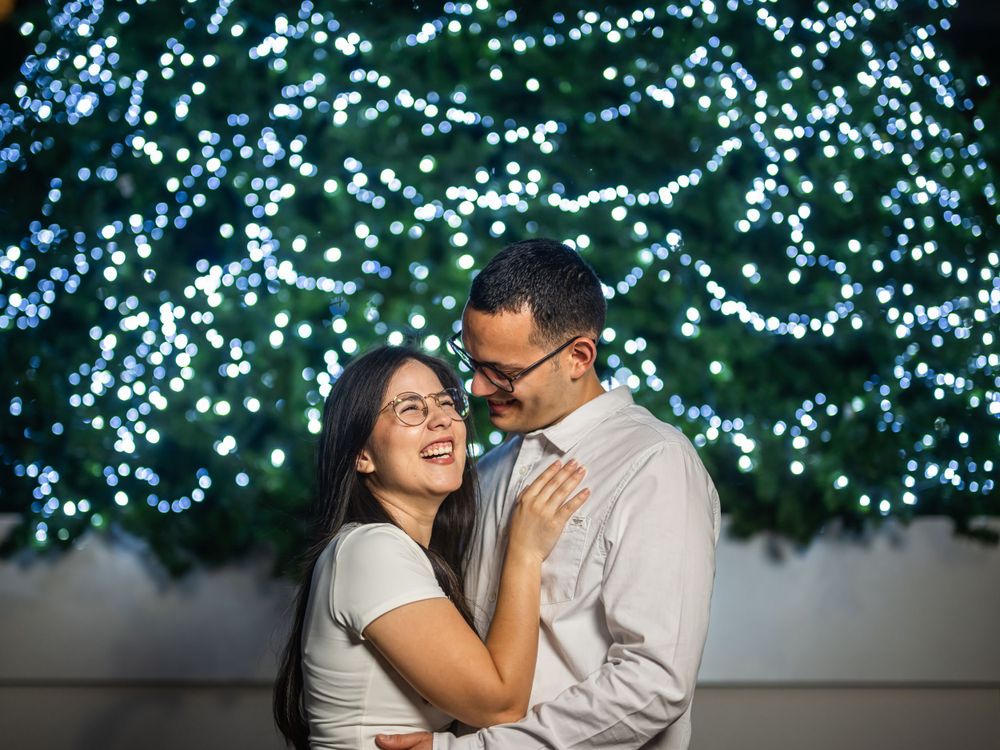 Couple standing together at night with glowing blue Christmas lights creating a magical backdrop.