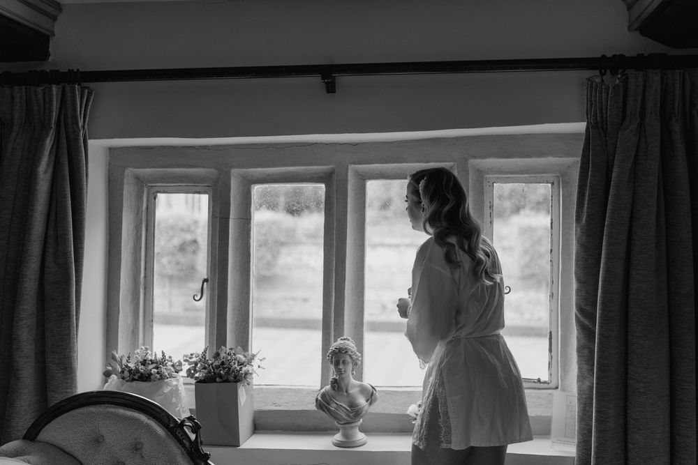 a black and white image of bride leaning and looking out of the window of oxnead hall in Norfolk