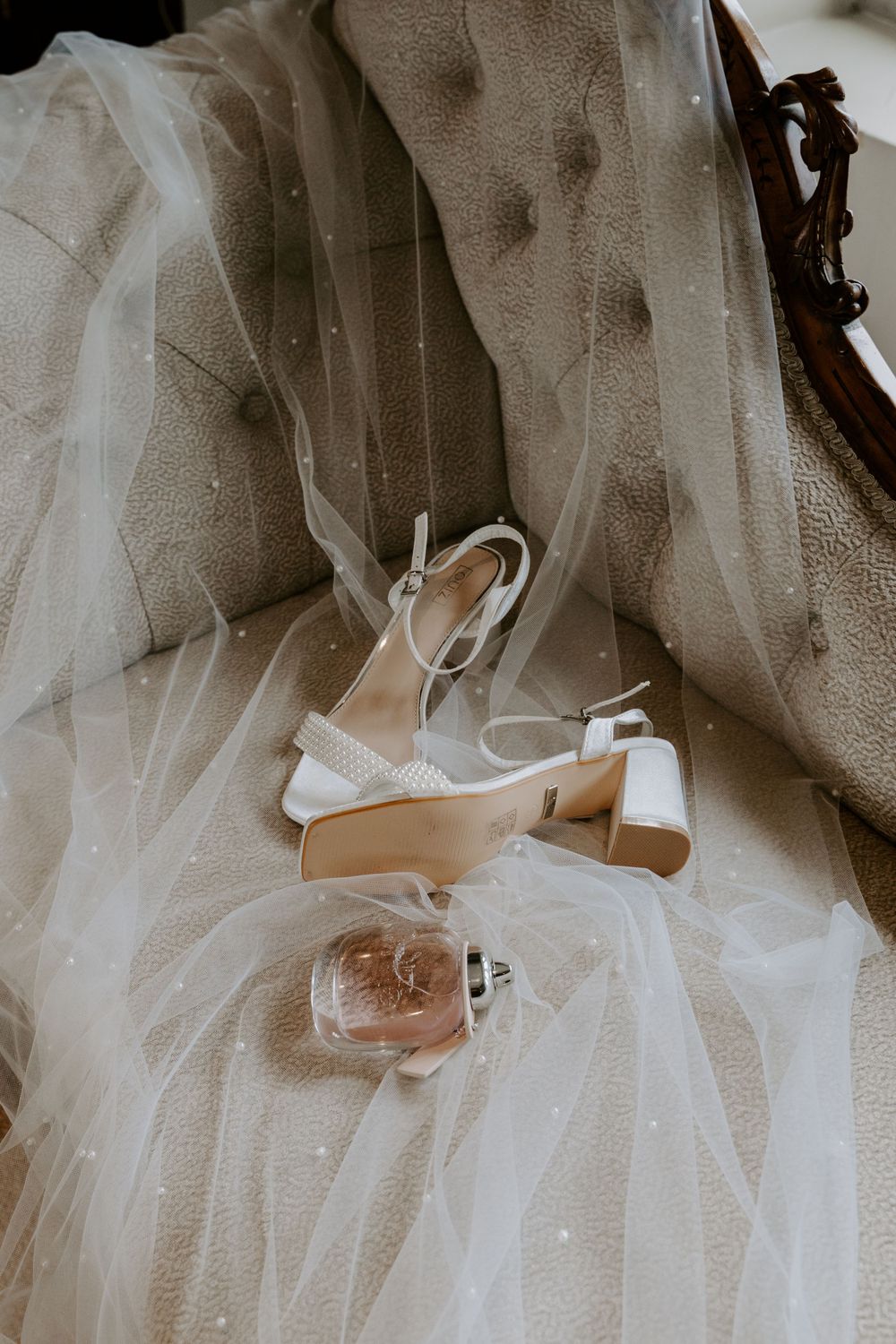 a pair of wedding shoes are laid on a wedding veil on a chaise lounge.