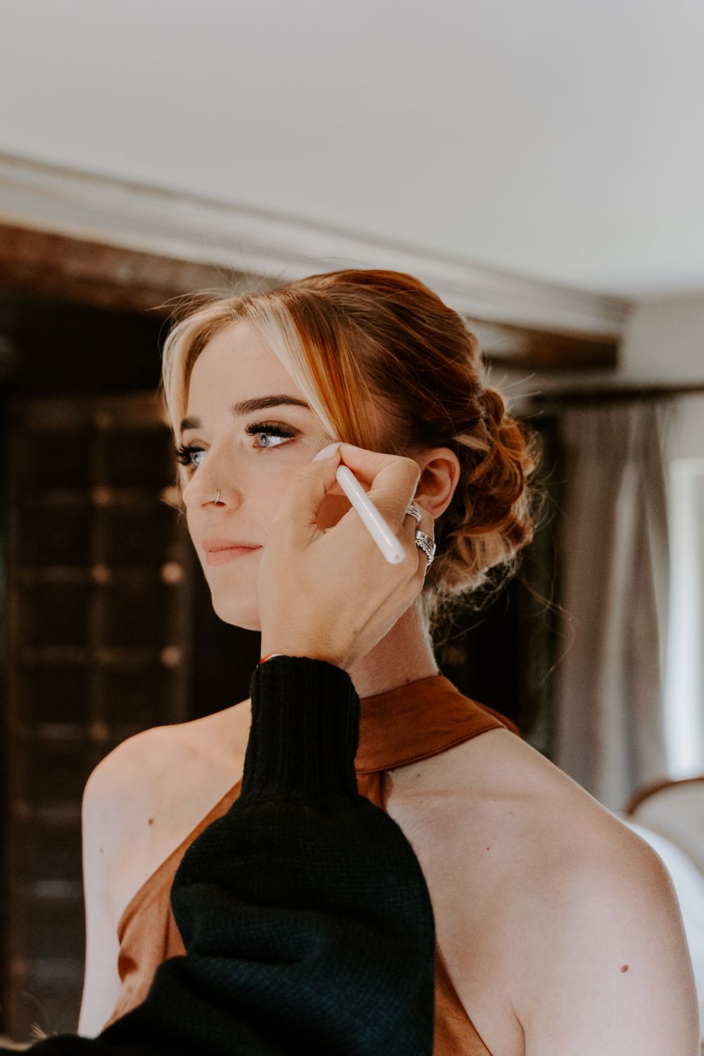 bridesmaid is having finishing touches to her makeup. MUA is adding face powder to her cheek bones with a brush.