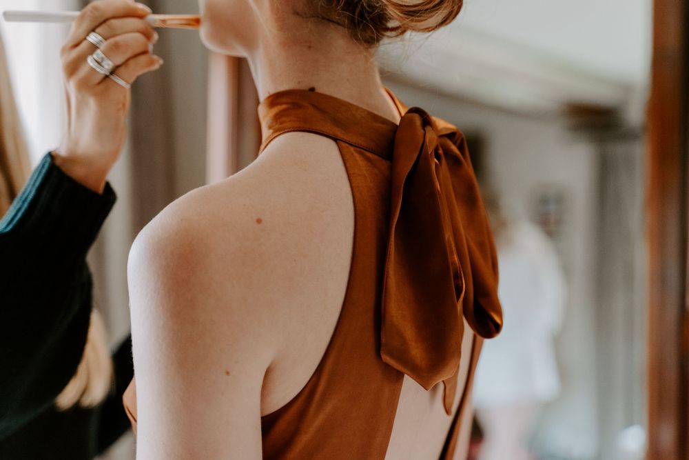 a close up the back of a bridesmaid dress. a burnt orange bridesmaid dress with a large bow at the back of the neck.