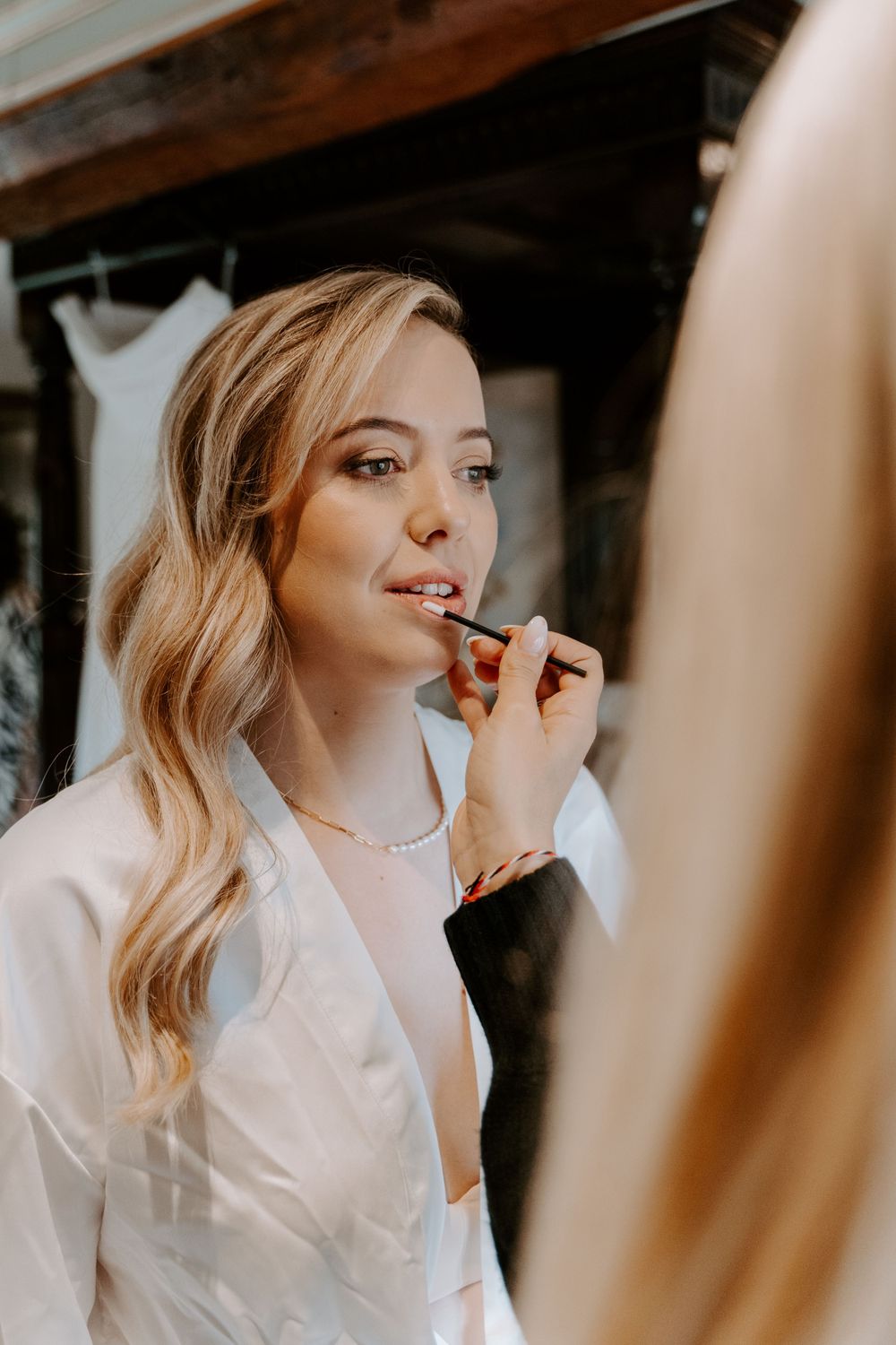 MUA is applying lipstick to a bride on her wedding morning.