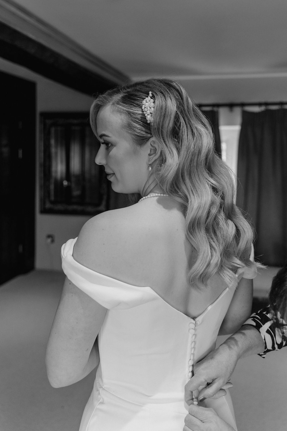 a close up image of the back of a brides dress. dress is off shoulder and figure hugging with buttons all the way down the back.