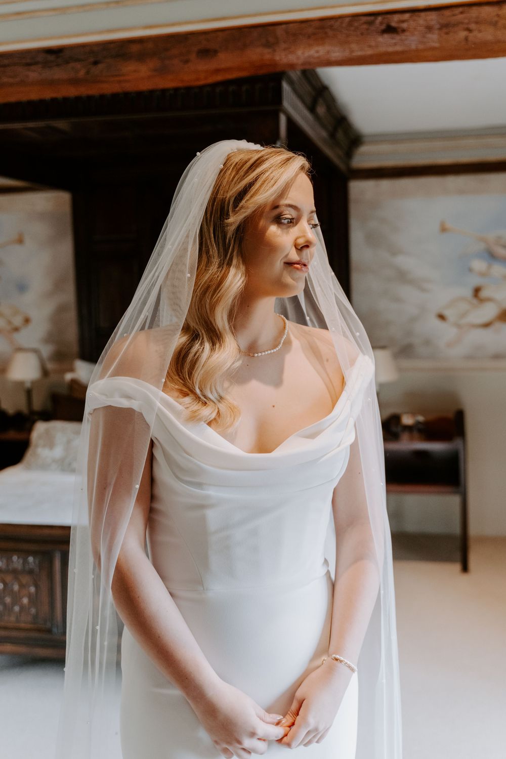 a bride wearing a figure hugging ivory gown, a veil and is looking to her left side.