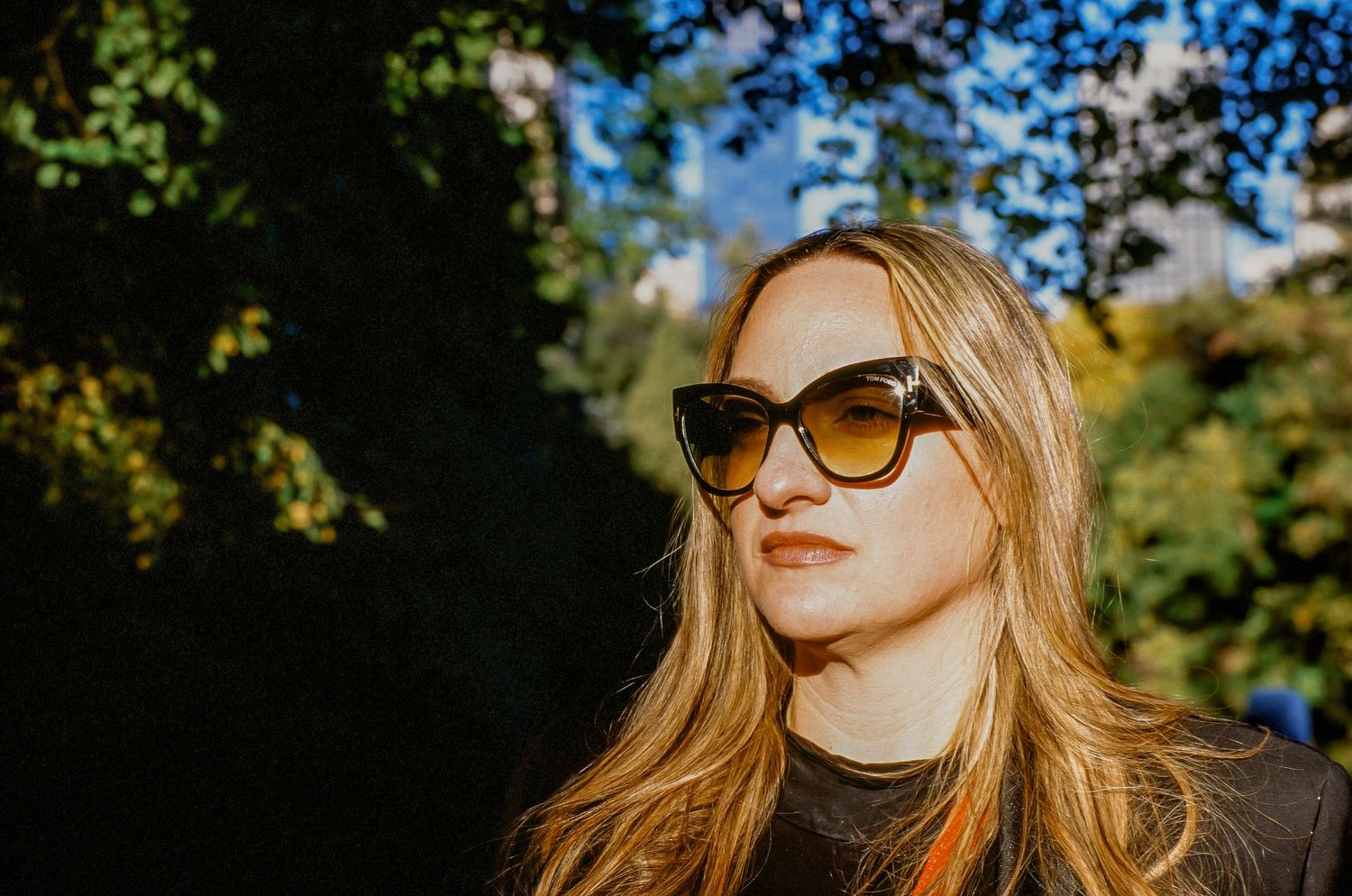 Portrait of person wearing sunglasses in warm sunlight with trees in background.