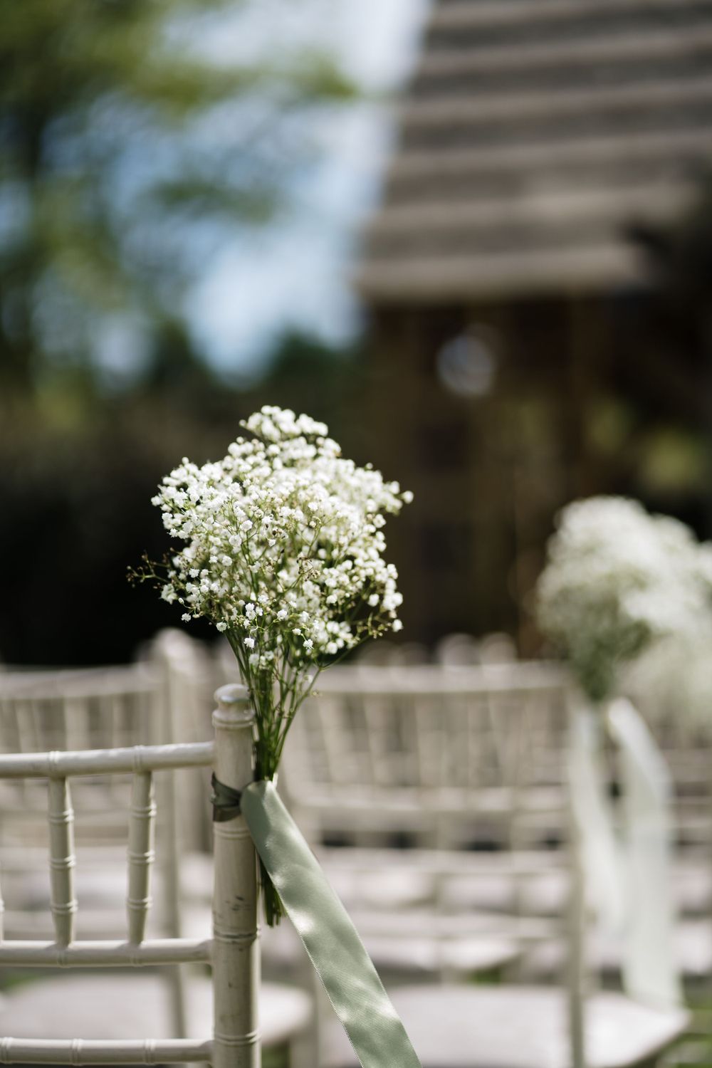 Delicate baby's breath flowers in a vase decorate a ceremony aisle chair.