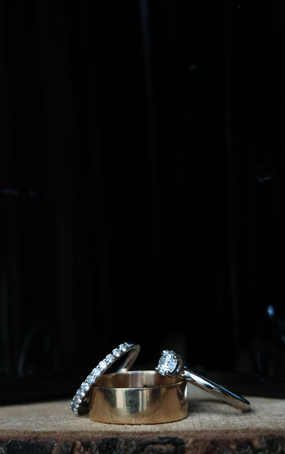 Wedding rings displayed on a rustic wooden surface with dramatic lighting.