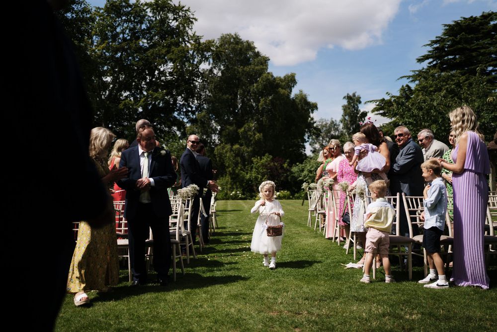 Wedding guests line a garden path as flower girls walk down the aisle.