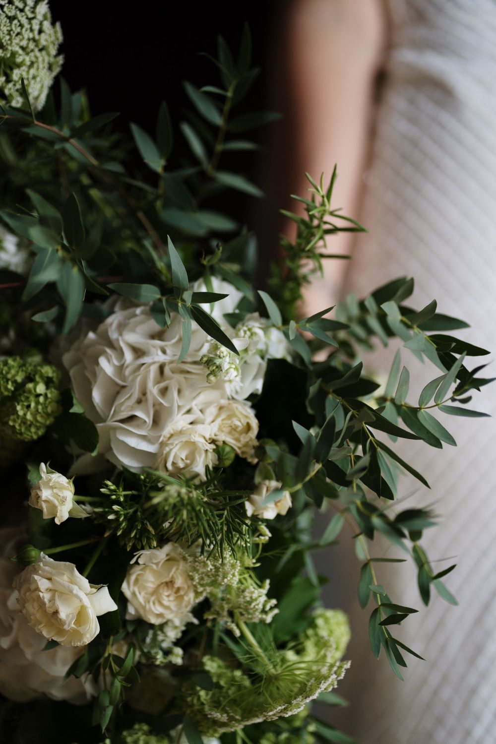 Elegant white wedding bouquet with roses and green foliage arranged in a rustic style.