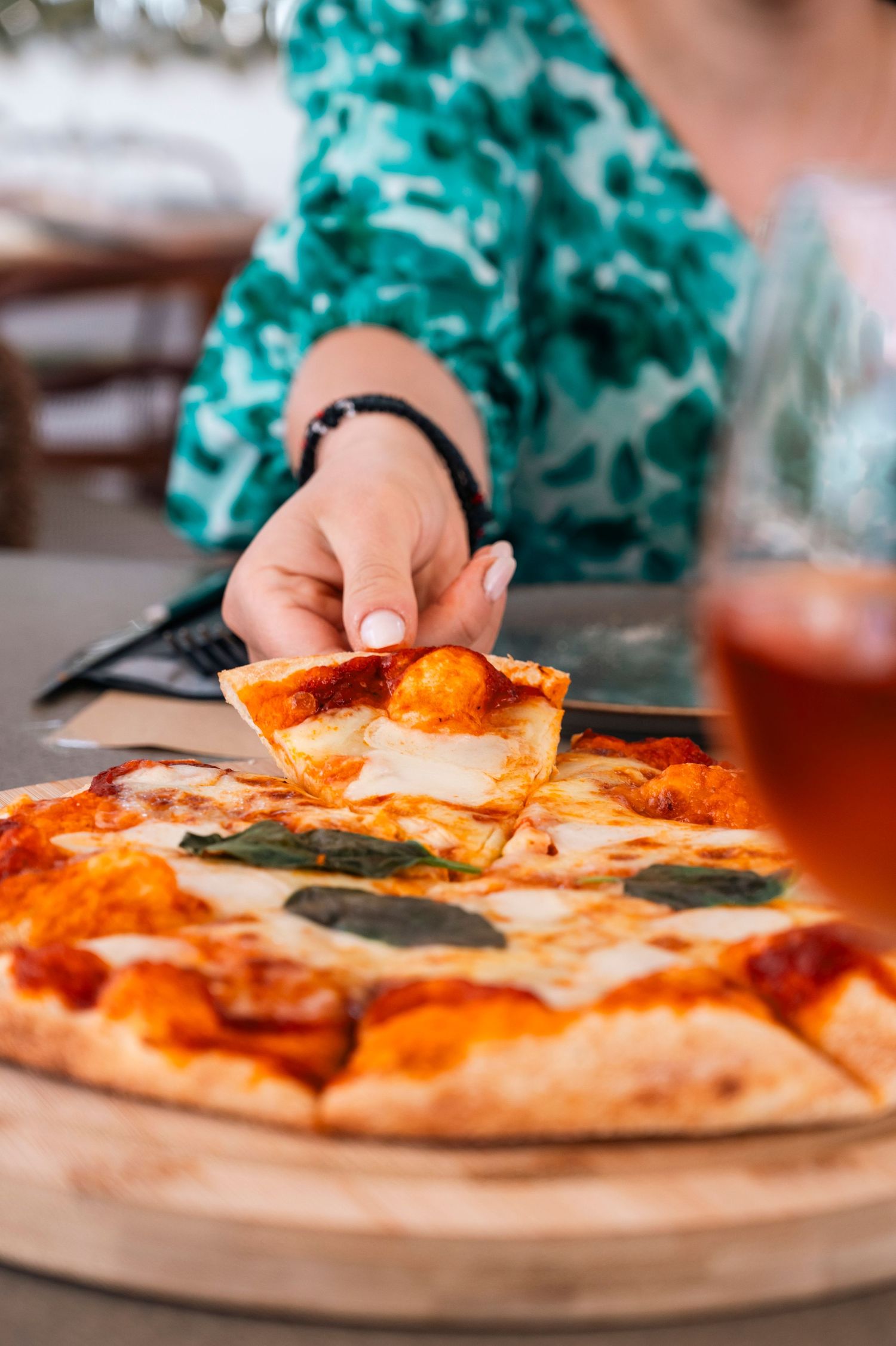 Close-up of hands reaching for a slice of margherita pizza on a wooden board.