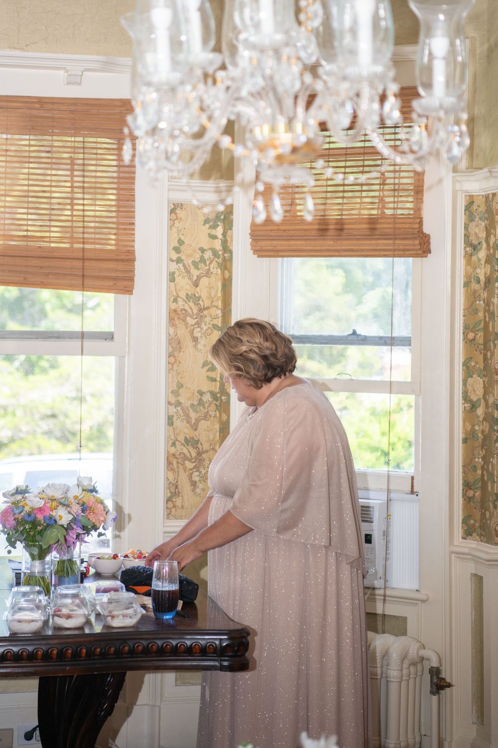 People in vintage-style dresses preparing refreshments in an elegant dining room.